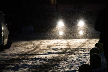 snowflakes during snowfall lit with light from car headlights at night on a road