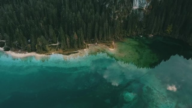 Aerial: Tracking shot of a mountain lake shore with alpine forest