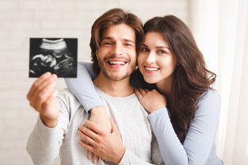 Happy millennial couple holding ultrasound scan of their expecting baby