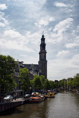 View of canal cruise tour boats, Westerkerk church's tower, trees and historical, traditional buildings. It is a sunny summer day.