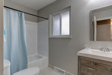 Small bathroom in new model home with window, blue shower curtain, and contemporary cabinet, sink, and fixtures