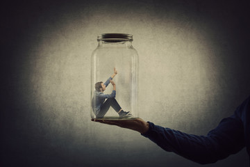 Business concept with a scared tiny man trapped inside a glass jar held by his gigantic boss hand....