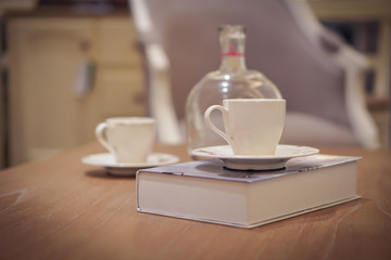 Focus selection: A white coffee cup placed on a book at a table and a glass bottle near it. In a light, comfortable atmosphere