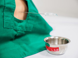 Close-up detail of a physician collecting spinal fluid from a pediatric training dummy using a lumbar needle. Healthcare and medical education concept. - 306958370