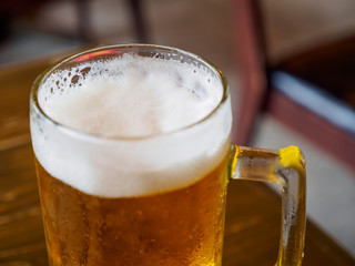 Wide closeup of a beer stein containing ice cold lager with a foamy head. Shallow focus. Bangkok, Thailand. Travel and party.