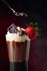 Coffee drink with whipped cream, strawberry and pieces of black chocolate on a dark background.