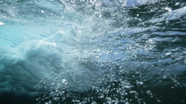 Underwater footage of a breaking wave with a surfboard seen from the water.