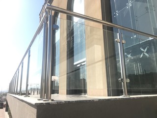 An Stainless steel glass transparent handrails with hairline finish fixed at lobby or entrance of multistory buildings and sky background visible with white clouds