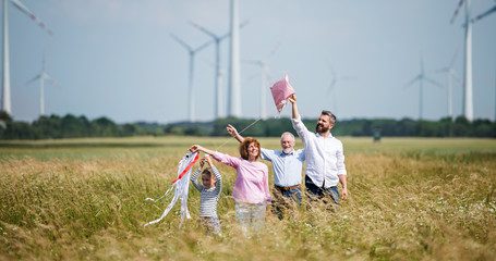 Multigeneration family standing on field on wind farm, playing with kite.