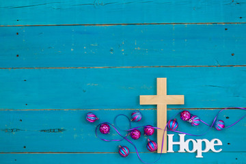 Wood cross with the word Hope hanging on antique rustic teal blue wooden sign with colorful turquoise and pink glass Christmas ornaments; religious holiday and spiritual background with copy space