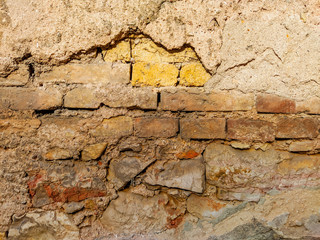 Old and ruined wall facade outside of a house with bricks and cement showing and sunlight lighting the wall with no pattern and rough texture
