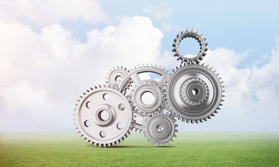 Abstract mechanism with cogwheels on green meadow