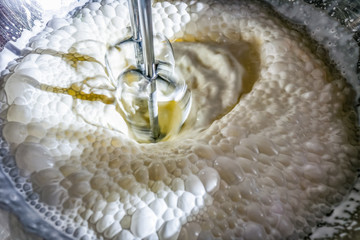 Whipping cream with an electric mixer....close-up with dramatic shadows and bubbles swirling in a...