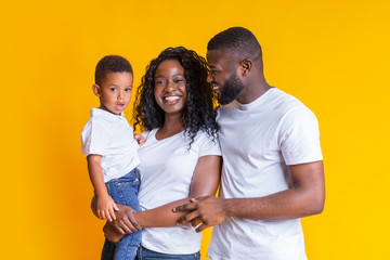Happy black family with little son smiling and hugging on yellow background