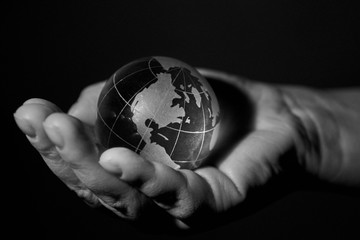 Glass globe, planet Earth, in the hands of a woman, black and white photo.