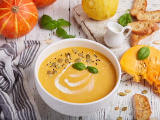 Bowl of pumpkin and carrot cream soup with seeds and basil leaf. Vegetarian homemade dish