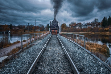 Fototapeta na wymiar An ancient steam locomotive rides the rails of a railway on an embankment in gloomy autumn weather