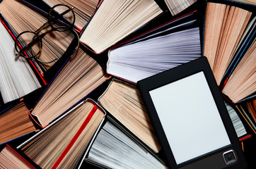 The e-book with a white screen lies on the open multi-colored books that lie on a dark background, close-up