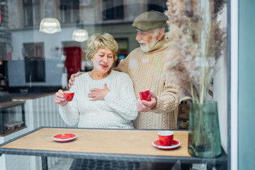 Happy senior couple having anniversary day, bearded husband holding a ring and kissing for his wife in cheek. Feel of happiness.