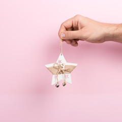 Male hand on a pink background holding Christmas tree decoration. Christmas concept symbol, commercial bucket print, copy space.