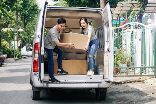 Excited Young Boyfriend And Girlfriend Taking Cardboard Boxes With Belonging Out Of Truck When Moving In New Apartment