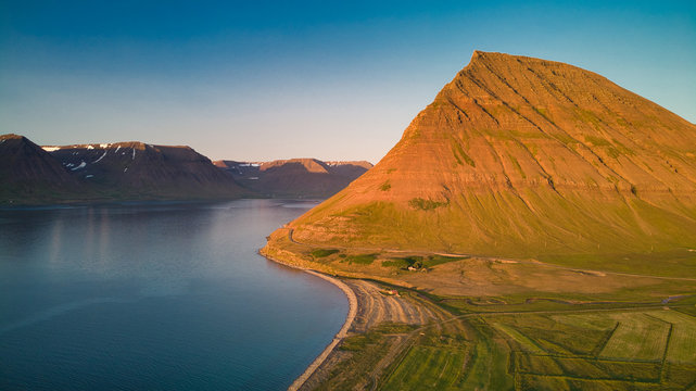 High aerial view of a stunning green valley with a river surrounded by large mountains in Westfjord. Midnight sun, Iceland