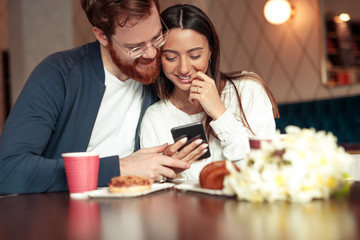 Cheerful couple using smartphone in cafe