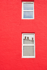 fachada pintada de rojo con dos ventanas pintadas de blanco con reflejos en los cristales