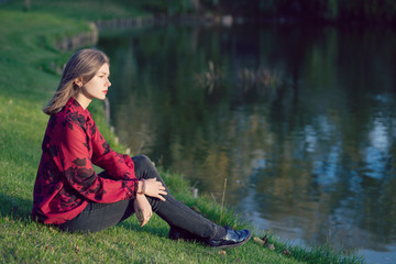 Girl sitting on green grass near the lake at sunset