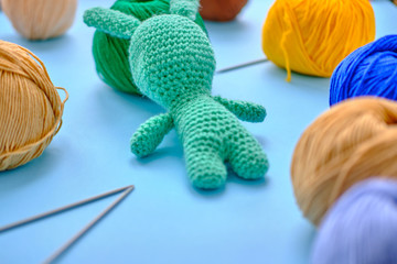 Bright color yarn clews with pastel green stuffed bunny on the blue background. Concept of amigurumi toy making, handcrafting, knitting, hobbie
