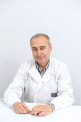 Portrait of a professional male doctor in a white coat sitting at a table