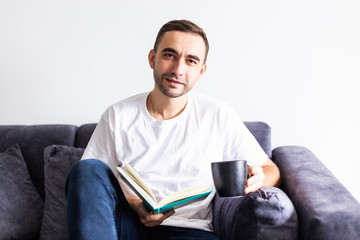 Young handsome man having coffee while reading book in living room