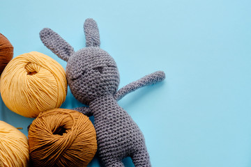 Bright color yarn clews with grey stuffed amigurumi bunny on the blue background. Concept of amigurumi toy making, handycraft, knitting, hobbie