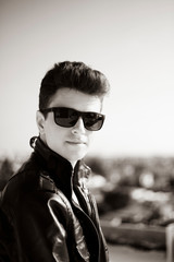 Young attractive man posing in front of camera in a dark  brown jacket on the roof of a residential building