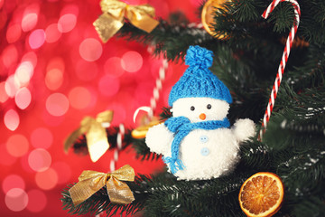 Christmas fir tree with small snowman, candies and dry oranges on blurred lights background