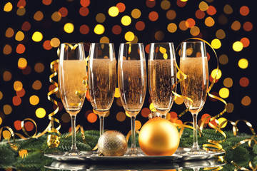 Glasses of champagne with christmas baubles, ribbon and fir tree branches on blurred lights background