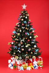 Christmas fir tree with ornaments and gift boxes on red background