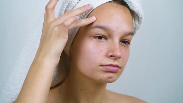 Teenage girl with bath towel on head examining her face