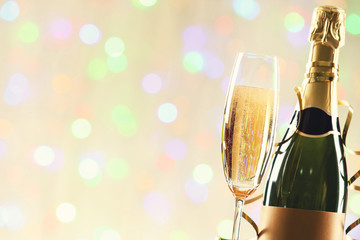 Bottle and glass of champagne with ribbon on blurred lights background