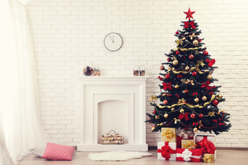 Christmas fir tree with ornaments and gift boxes near fireplace at home