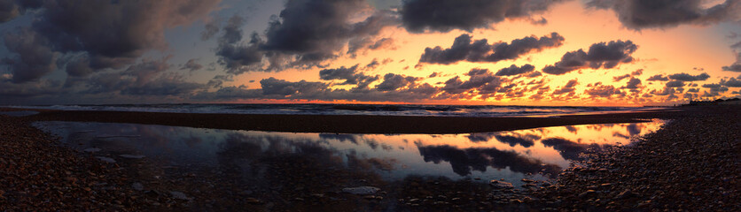 Amazing golden hour on the pebble beach with dramatic sky reflections on sea water and fantastic lights