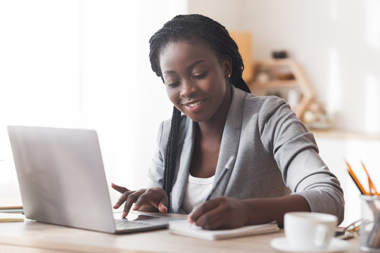 Black businesswoman working in office, typing on laptop and taking notes