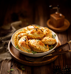Baked dumplings (pierogi) with mushroom stuffing in a ceramic bowl on a wooden table, close-up. ...