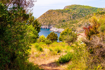 Fototapeta na wymiar Scenic landscape view from the overgrown rocky mountains of Cilento and Vallo di Diano National Park in Campania, Italy on hidden Cala Bianca beach surrounded by rocks in Tyrrhenian sea