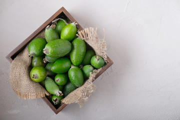 A new harvest. Feijoa in a wooden box with a burlap on a grey concrete background.