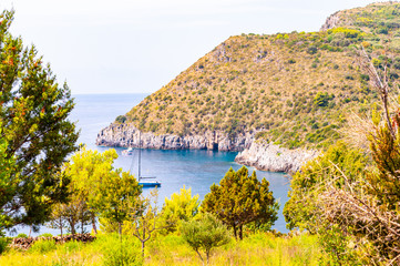 Scenic landscape view from the overgrown rocky mountains of Cilento and Vallo di Diano National Park in Campania, Italy on hidden Cala Bianca beach surrounded by rocks in Tyrrhenian sea