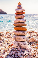 Fototapeta na wymiar The tower of flat stones on the beach. Stone balancing is the art discipline, or hobby in which rocks naturally balanced on top of one another in various positions. Cala Bianca Italy