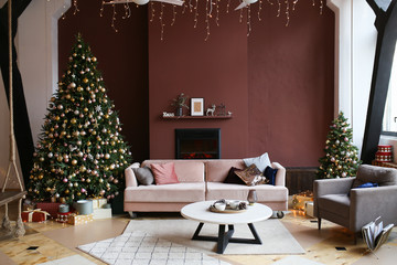 Christmas interior and decor. Modern spacious cozy living room with fireplace, dark walls, with a light soft sofa and coffee table, decorated with Christmas trees, gifts, garlands.