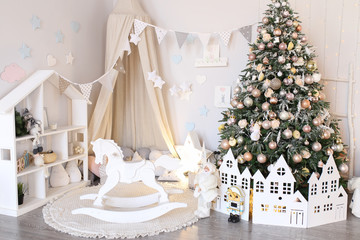 Christmas decor children's room. Bright, white, cozy room decorated with Christmas tree, canopy, horse and garlands.