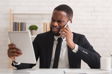 Unhappy manager working with tablet and talking by smartphone